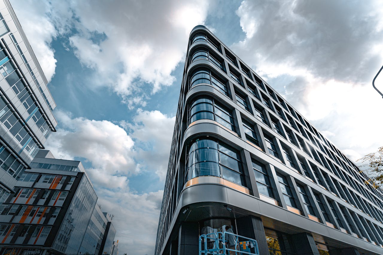 who-we-are Low angle view of a modern office building with a sleek glass facade against a cloudy sky.
